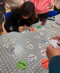 Choir member Jina writes her name on a handmade fabric nametag, on a table filled with other colourful name tags.